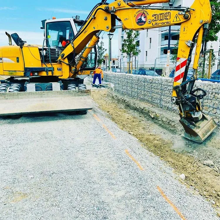 Machine de chantier effectuant des travaux de nivellement sur un trottoir pour un projet de voirie.