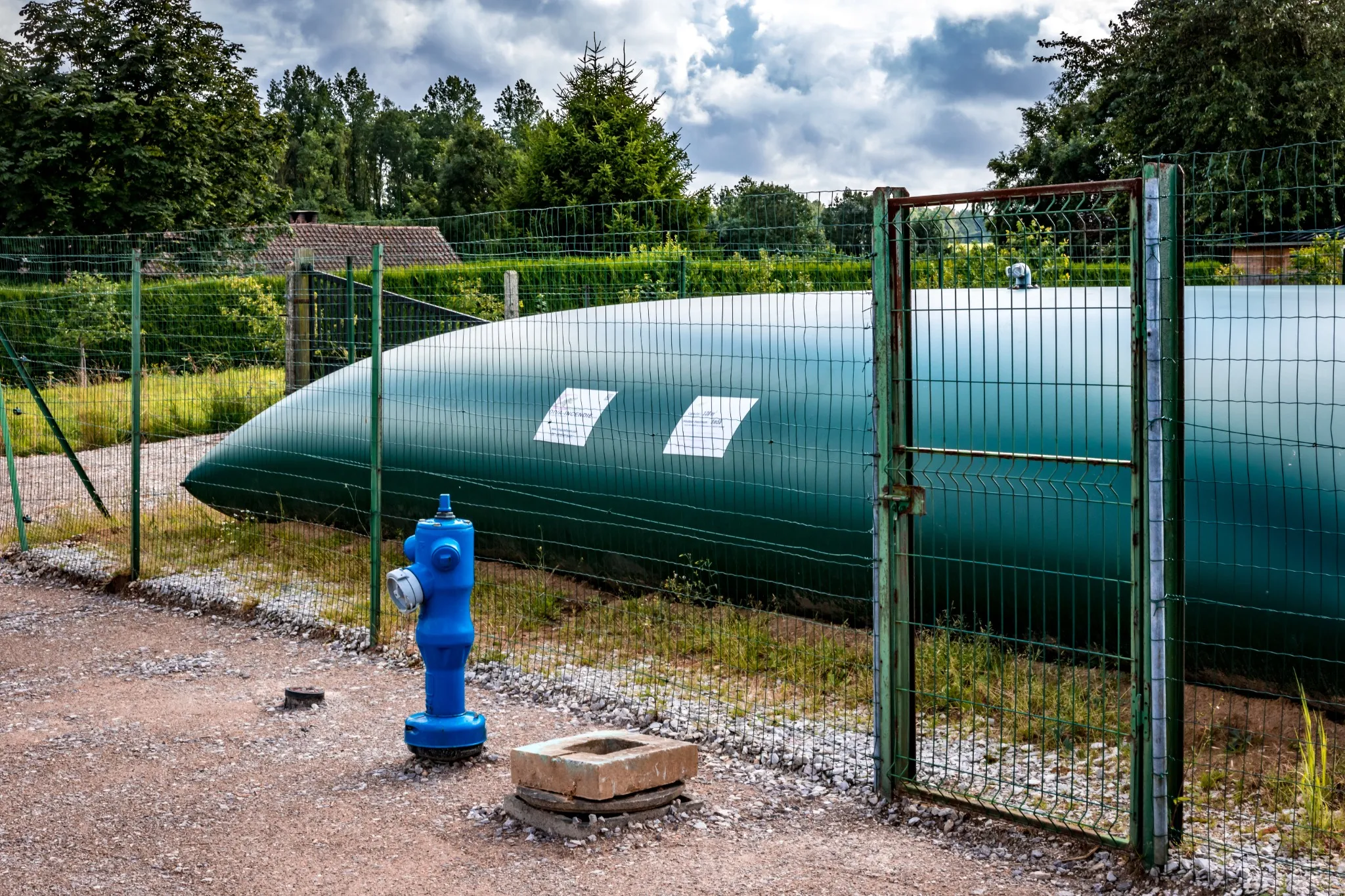 Réserve incendie sous forme de bâche gonflable verte avec un poteau d'incendie à proximité, sécurisée par une clôture.