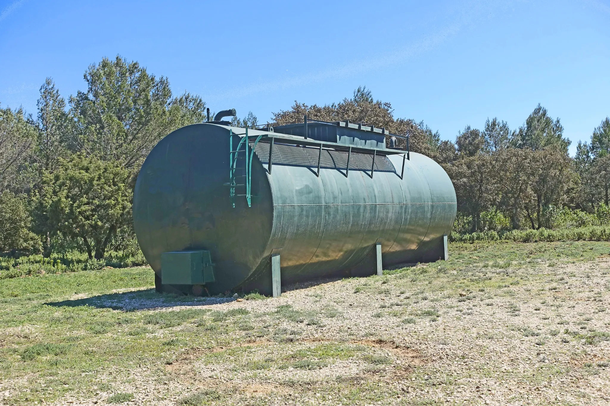 Grande citerne verte de réserve incendie installée en plein air, entourée d'arbres.