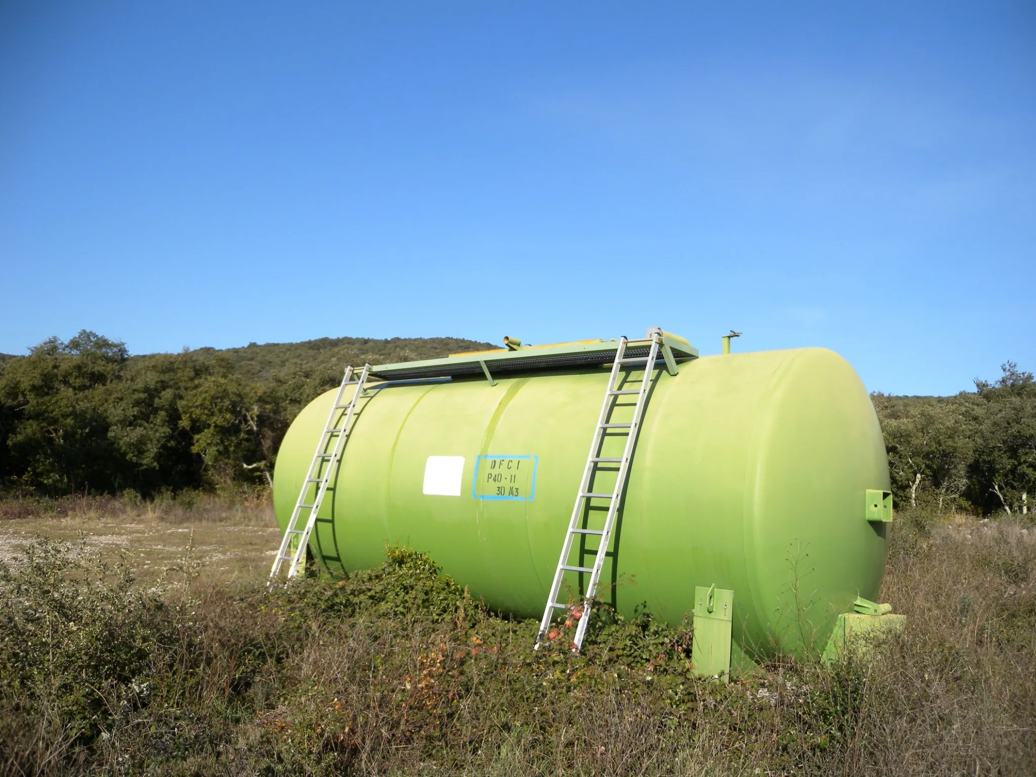 Réservoir de réserve incendie vert avec une échelle et des inscriptions, situé dans un champ. ​​