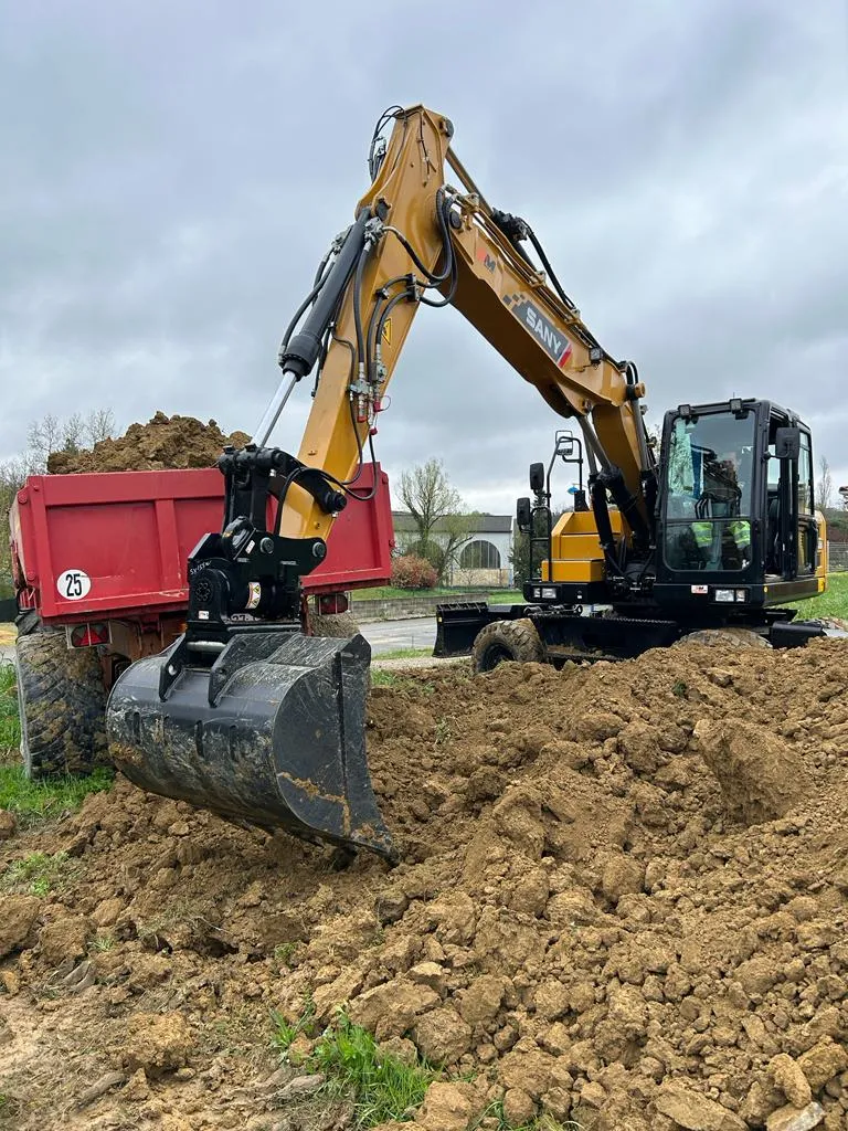 Excavatrice déplaçant de la terre dans un camion lors d'une opération de terrassement sur un terrain dégagé.