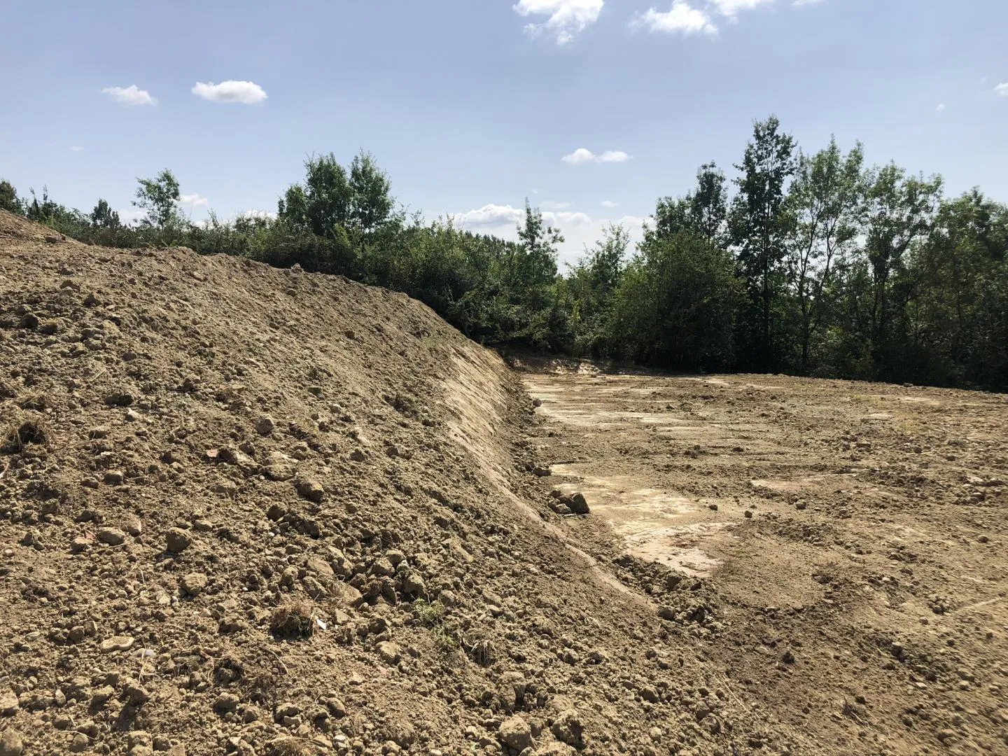 Terrain de terrassement nivelé, prêt pour la prochaine étape de construction, entouré de végétation.